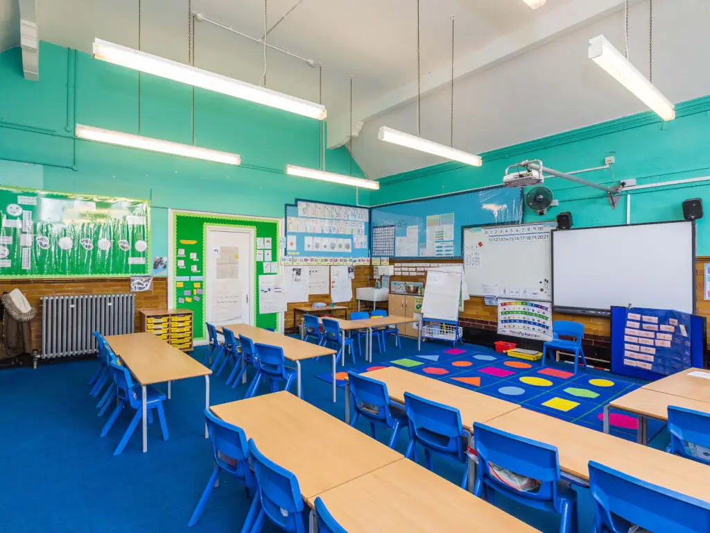 Modern classroom with blue chairs, wooden tables, and educational posters on green walls.